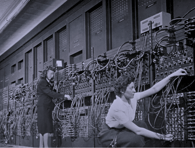 Mujeres Frente a computadoras primitivas con muchos cables